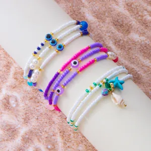 Boho-Fußkettchen-Set mit bösem Blick, bunten Perlen, Seestern und Muschel auf Sandhintergrund