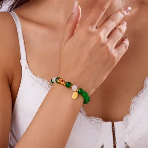 Close-up of green and white beaded bracelet with gold zodiac snake charm on a wrist.
