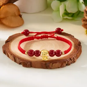 Gros plan d'un bracelet tressé rouge avec breloque serpent dorée et perles
