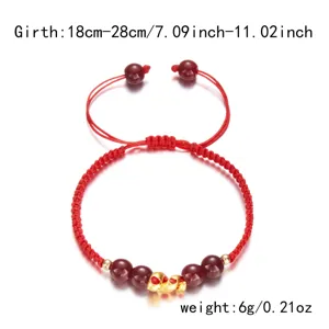 Détail d'un bracelet tressé rouge avec breloque serpent dorée et perles de cinnabre