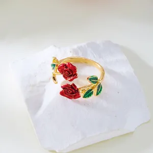 Detailed view of an elegant gold-plated open ring with red enameled roses and green leaves.
