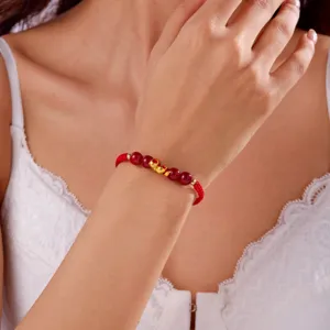 Gros plan d'un bracelet tressé rouge avec breloques serpent dorées et perles de cinabre.