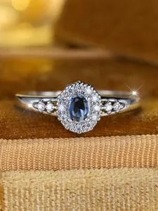 Makro-Detailansicht eines saphirblauen ovalen Zirkonrings mit Diamant-Halo-Einfassung in Silber
