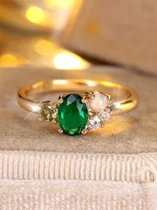 Close-up of gold jewelry ring with oval emerald-green stone and opal cluster detail