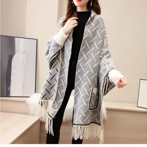 Dettaglio di un poncho grigio in maglia da donna con nappe e motivo geometrico in stile accogliente.