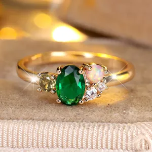 Elegant gold ring with oval green gemstone and opal accents on velvet background