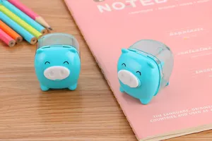 Close-up of cute blue pig pencil sharpeners on a pink notebook with pencils