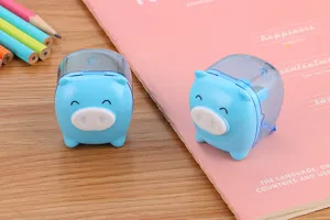 Close-up of two cute blue pig-shaped manual pencil sharpeners on a pink notebook