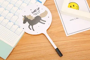 Close-up of cute cartoon unicorn fan pen on a wooden desk with stationery accessories