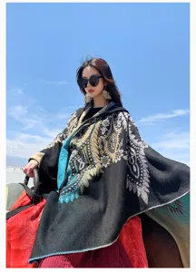 Asian model wearing a black ethnic knit poncho shawl against a clear blue sky background.