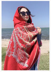 Vibrant red bohemian paisley hooded knit shawl worn by a model on a sunny beach.