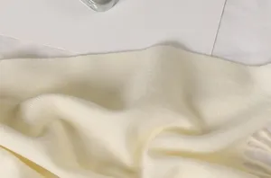 Makroansicht der weichen Stricktextur und Fransen eines cremefarbenen Kunstkaschmirschals
