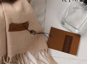 Detailaufnahme eines beigen Schals aus Kaschmirimitat mit Fransen und GERUNSI-Markenlabel.