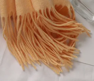 Nahaufnahme der weichen Fransenquasten eines orangefarbenen Schals in Kaschmir-Optik.