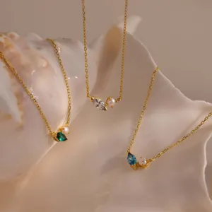 Close-up of gold necklaces with marquise birthstones and pearls on a shell.