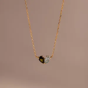 Close-up of heart-shaped pendant with green and light blue gemstones on gold chain.