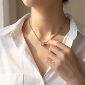 Detailopname van een zilveren ketting met tonvormige hanger en glimmende steentjes op model