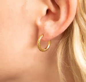 Close-up detail of a gold hammered titanium steel hoop earring worn on an earlobe.