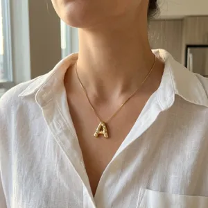 Primer plano de una modelo con un collar dorado con colgante de letra A y pequeñas piedras brillantes