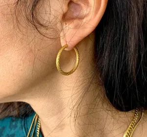 Macro detail of textured golden titanium steel hoop earring worn on model's ear