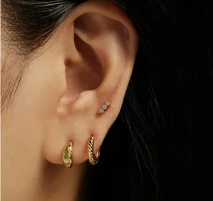 Titanium steel gold earrings set on ear with green stone and twisted texture close-up detail.