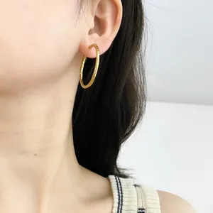 Detailed macro view of gold-finished titanium steel hoop earrings with textured pattern.