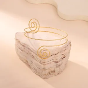 Vista dettagliata di un elegante bracciale da braccio a spirale dorato su pietra naturale.