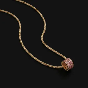 Gedetailleerde opname van een gouden vlechtketting met een roze edelsteen cilinder hanger