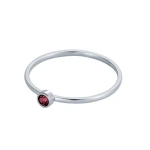 Détail d'une bague délicate en argent avec une pierre de naissance rouge ronde