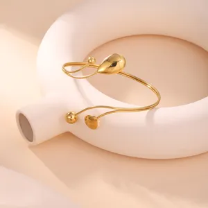 Elegante bracciale geometrico dorato con dettaglio a goccia su supporto decorativo.