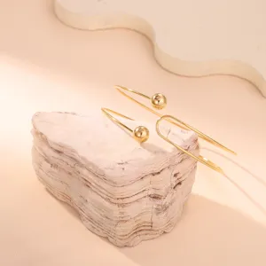 Dettaglio di un bracciale da braccio geometrico dorato minimalista su un supporto in pietra