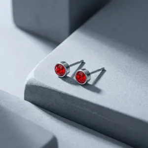 Detailed macro view of small silver stud earrings with vibrant round red zircon stones.