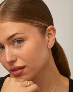 Detailopname van elegante ronde oorknopjes in lichtblauw en paars aan het oor van model