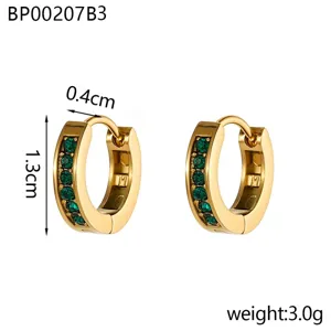 Détail des boucles d'oreilles huggie dorées avec une rangée de pierres pavées vertes.