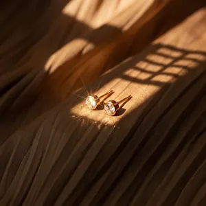 Macro view of gold-plated zircon stud earrings on pleated fabric with warm shadows