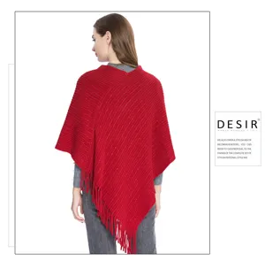 Détail du poncho en tricot rouge avec soie dorée scintillante et franges élégantes.