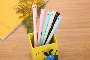 Close-up of cute cartoon cat cap gel pens in various pastel colors and a yellow holder.