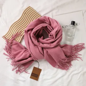 Lifestyle-Detail eines gemütlichen rosa Schals aus Kaschmirimitat mit Fransen auf Stoff.