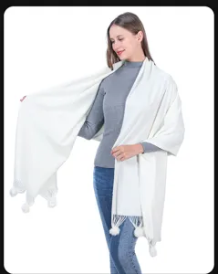 Detailansicht eines eleganten, weichen, weiß gestrickten Schals mit dekorativen Bommeln.