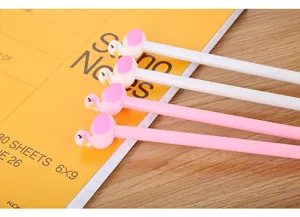 Gros plan sur d'adorables stylos gel flamant rose et cygne posés sur un carnet de notes jaune
