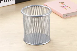 Detalle de un organizador de portalápices de malla metálica redonda plateada en mesa.