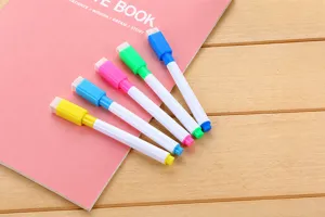 Close-up of five colored whiteboard markers with integrated eraser caps on pink notebook