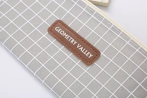 Close-up of a grey grid oxford cloth pencil case with GEOMETRY VALLEY leather patch.