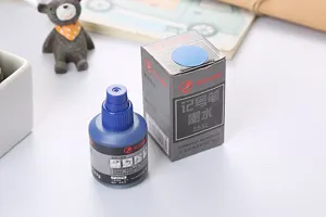Detalle de una botella de tinta azul para marcador permanente con caja en un escritorio