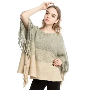 Detailed view of an oversized knit poncho featuring gray and beige color-blocks and long fringes.