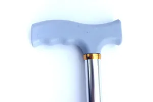Primo piano del manico del bastone, impugnatura ergonomica antiscivolo grigia, anello dorato.