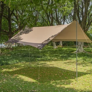 Détail de bâche de camping extérieure installée sur herbe verte avec poteaux solides.