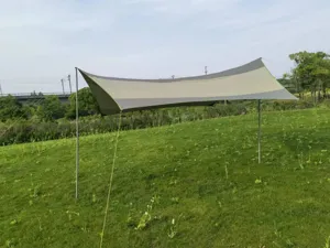 Détail de bâche de camping extérieure installée sur herbe avec des mâts et haubans.