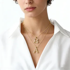 Close-up detail of layered gold letter pendant necklaces with sparkling zirconia stones.