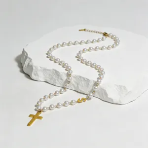 Nahaufnahme der eleganten Perlenkette mit goldenem Kreuz und einem Buchstaben S Anhänger.